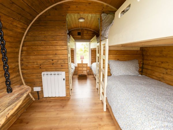 Wood-paneled room with bunk beds, wooden bench, and window at the far end letting in light.