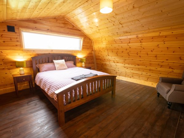 Cozy attic bedroom with wooden walls, a double bed, side tables, and an armchair.