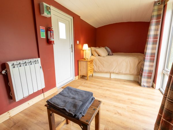 Cozy bedroom with a single bed, lamp, towels on a stool, and red walls.