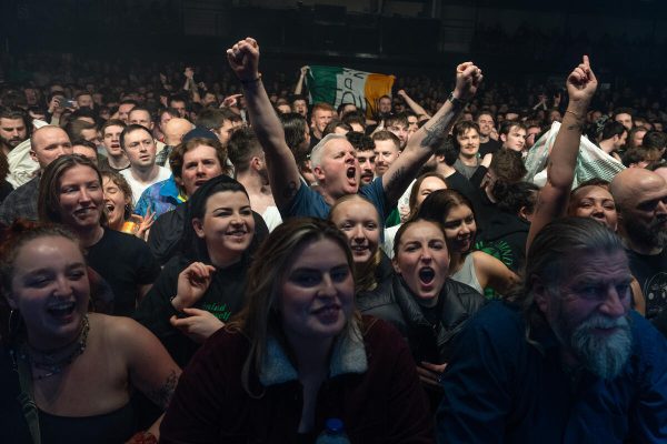 Crowd at a concert, cheering enthusiastically with an Irish flag visible in the background.