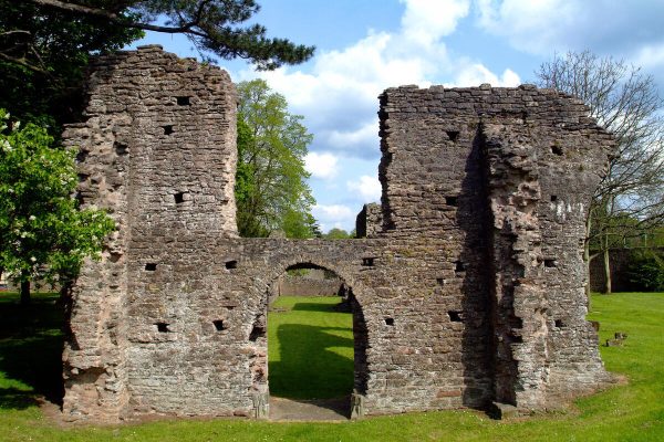 Ancient stone ruins with an arched doorway, surrounded by grass and trees under a blue sky.