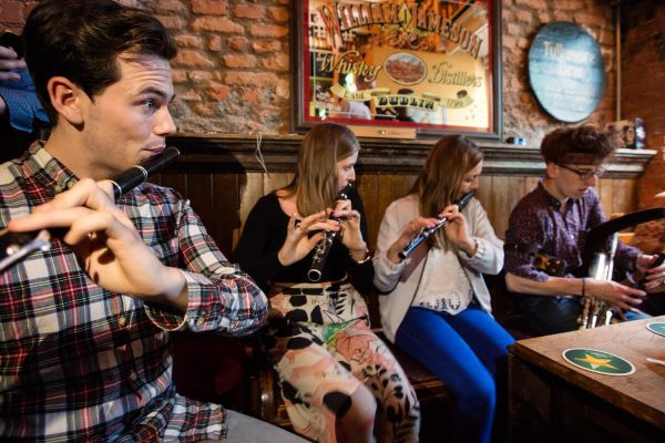 Four young musicians playing traditional instruments in a cozy pub with brick walls.
