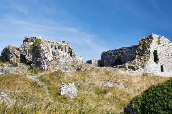 Ruins of an old stone building on a grassy hillside under a clear blue sky.