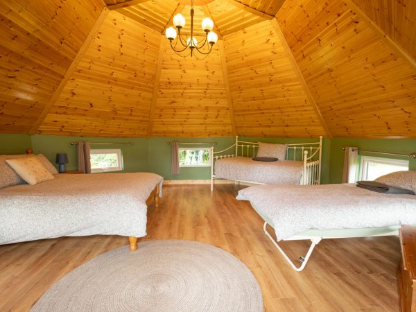 Cozy wooden room with three beds, chandelier, round rug, and small windows.