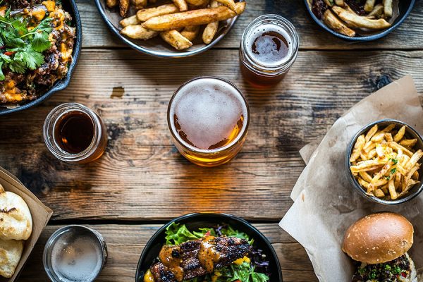 Overhead view of burgers, fries, salad, and beers on a rustic wooden table.